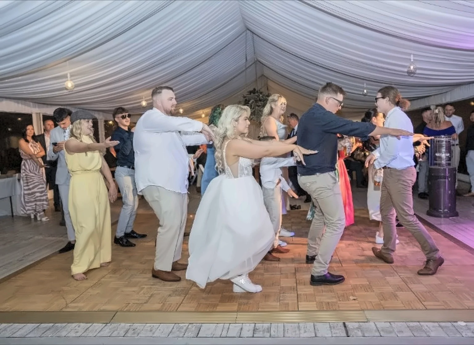 A group of wedding guests dancing together in a reception marquee