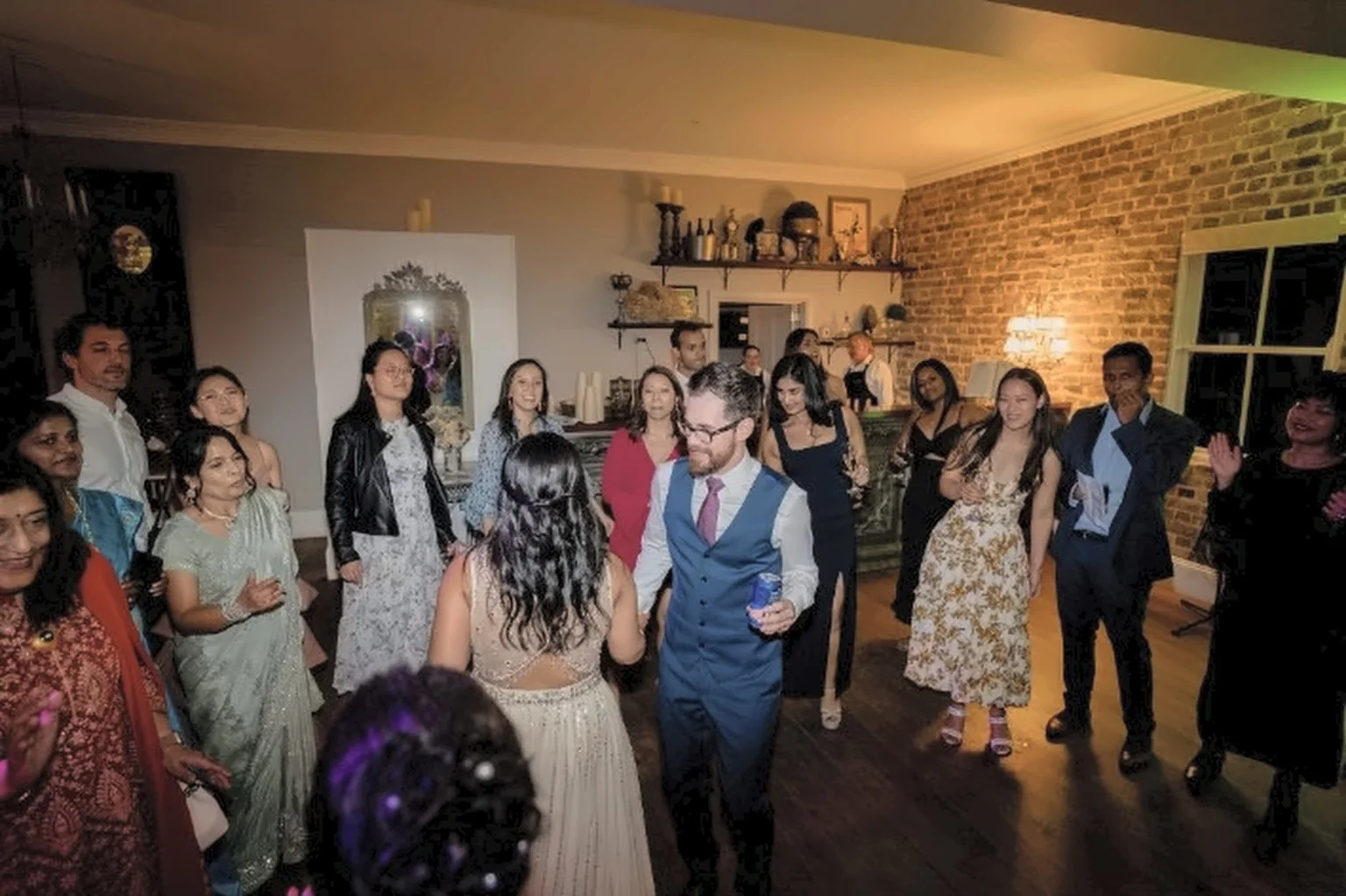 Wedding guests dancing together in a warmly lit brick reception venue