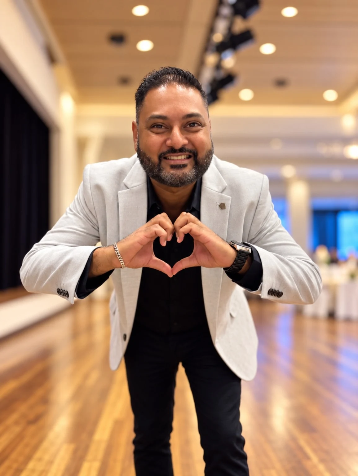 Nav smiling in a light grey blazer at an event, making a heart with his hands